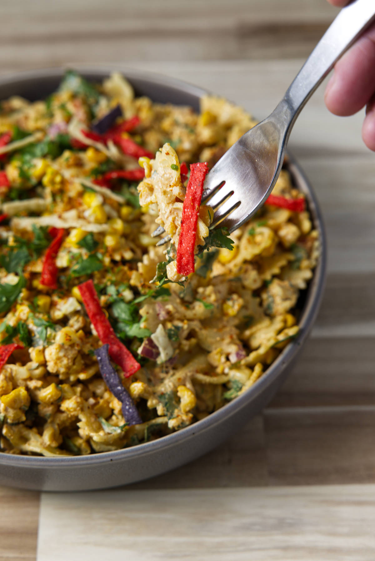 Fork with a bite of street corn pasta salad with brite red and purple tortilla strips and a sprinkling of cilantro.
