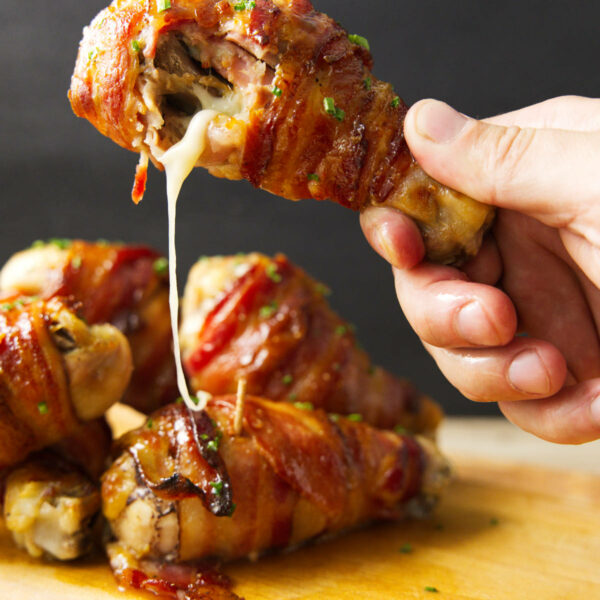 Holding a stuffed chicken leg with a bite taken out of it and melty cheese oozing out.