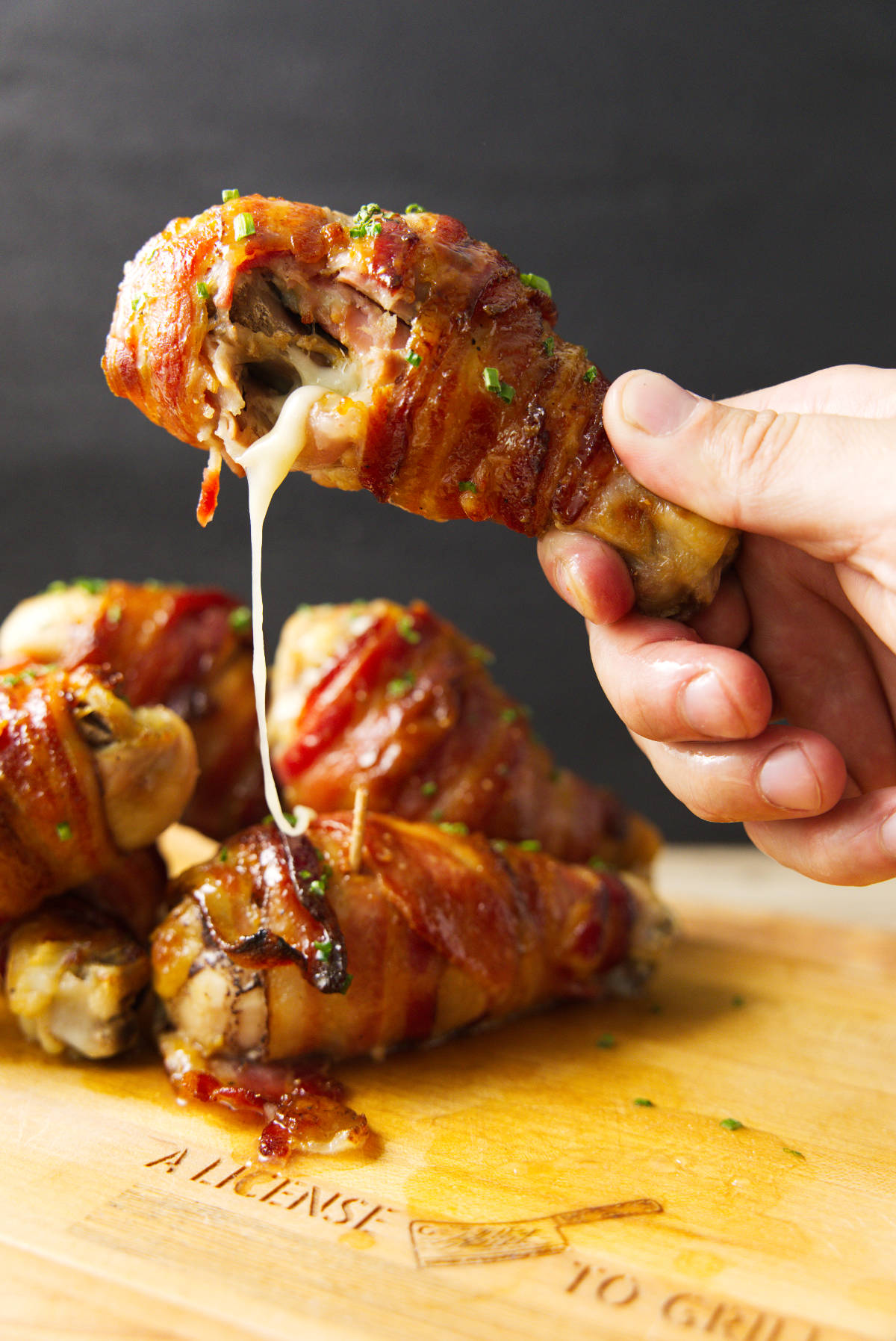 Holding a stuffed chicken leg with a bite taken out of it and melty cheese oozing out.