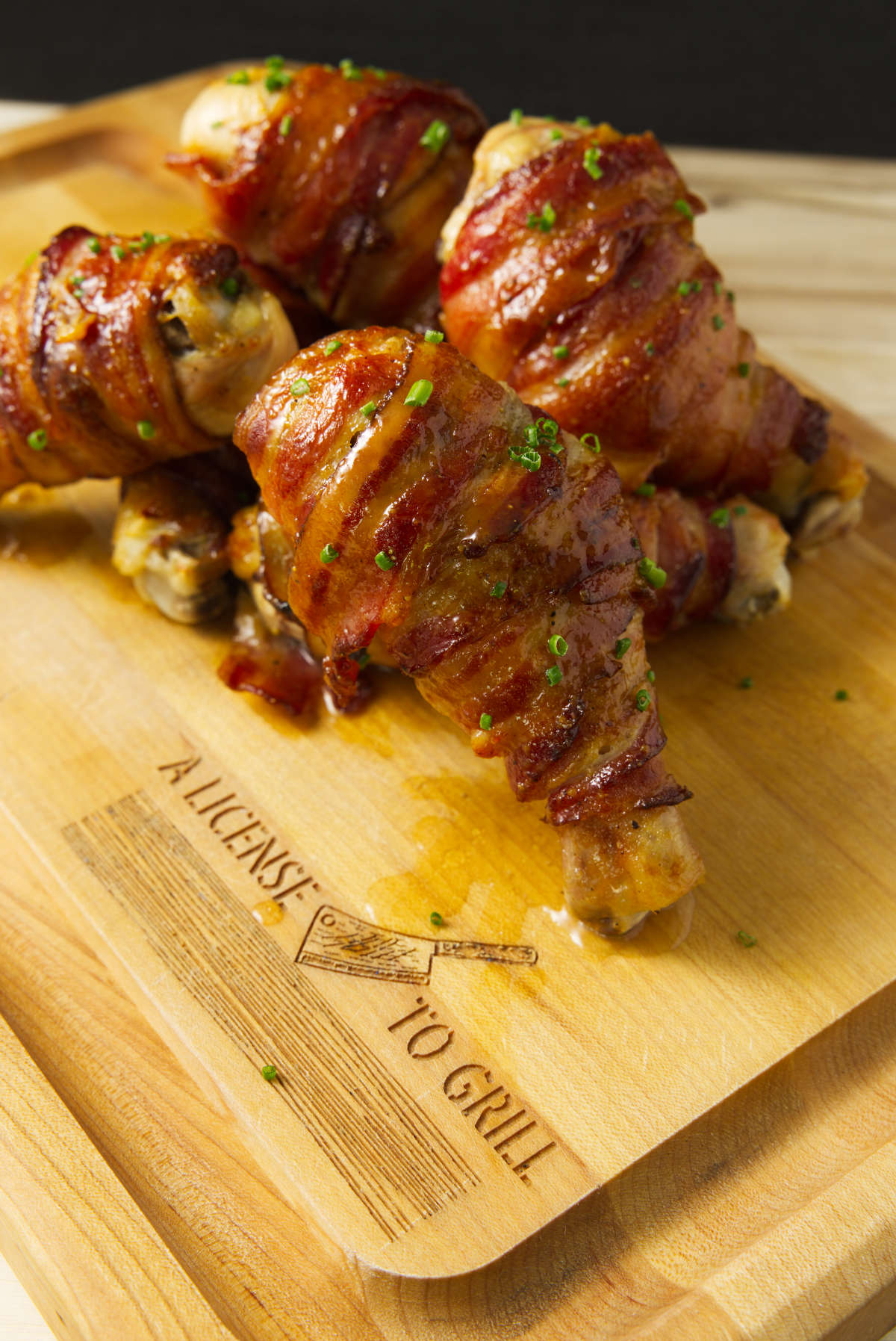 Bacon wrapped smoked stuffed chicken legs stacked on a cutting board.