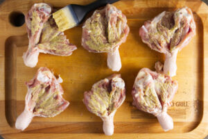 Brushing butterflied chicken legs with dijon mustard.