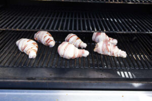 Bacon wrapped chicken legs on smoker grates.