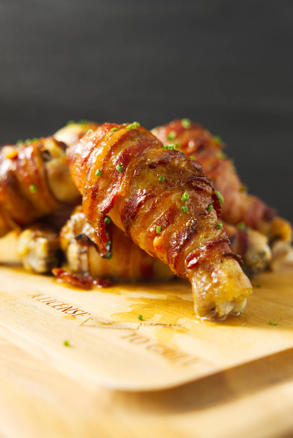 Chicken legs wrapped in bacon stacked on a cutting board.