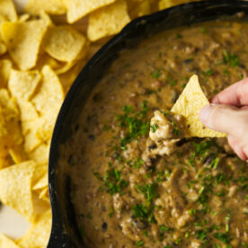 Chip being dipped in to large skillet of smoked cheese dip.