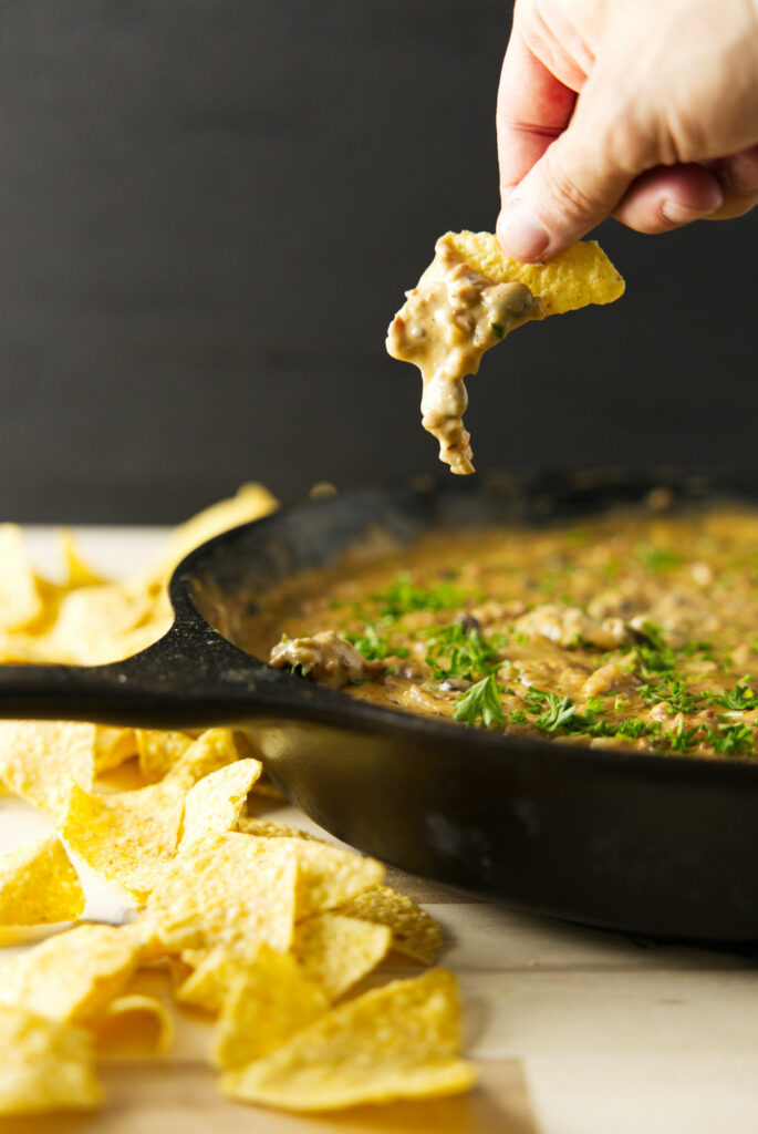 Gooey cheese dripping from chip with skillet of smoked cheese dip underneath.
