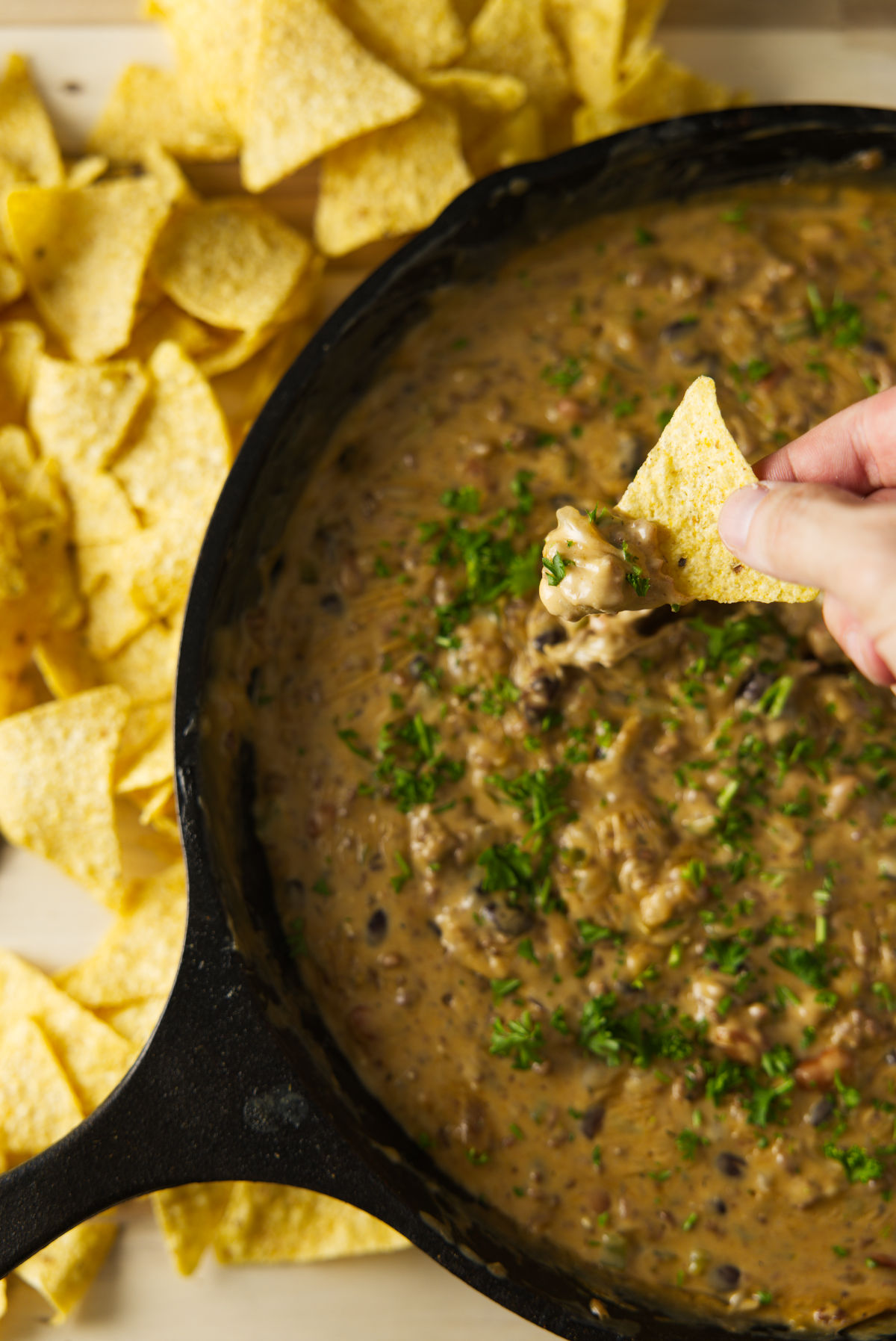 Dipping chip in to large skillet of gooey smoked chili cheese dip.