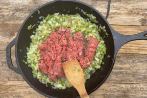 Large skillet with onions and green pepper with ground beef sautéing.