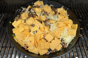 Large skillet filled with chili cheese dip on the smoker.
