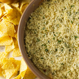 Smoked jalapeño popper dip with a bread crumb topping in a large bowl next to tortilla chips.