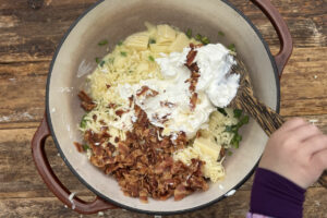 Mixing together smoked jalapeño popper queso dip in large dutch oven.