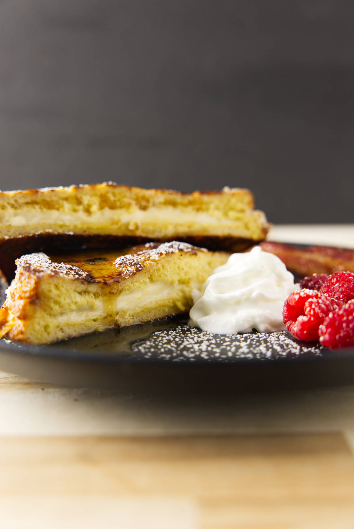 A stacked plate of French toast with whipped cream and raspberries.
