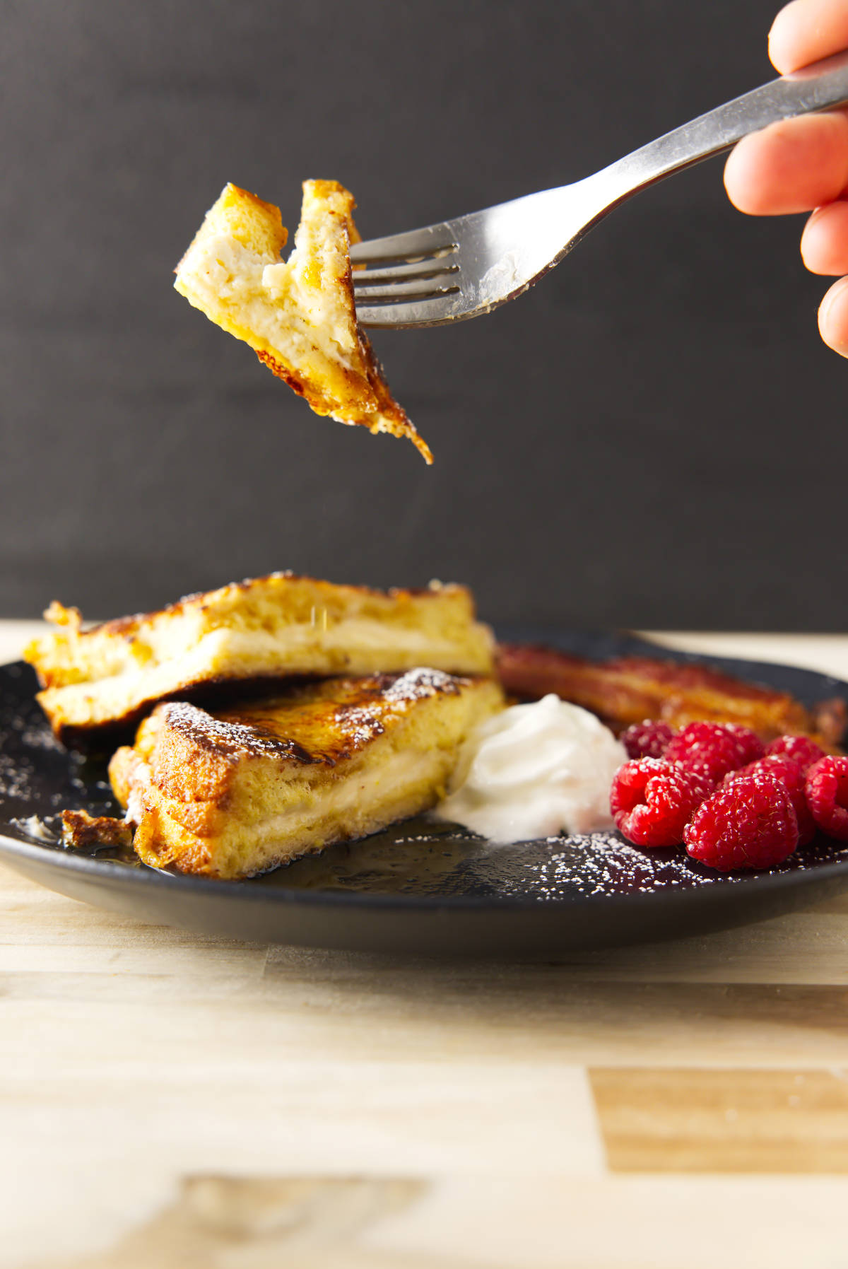 Fork with a bite of French toast on the end, hovering over the plate.