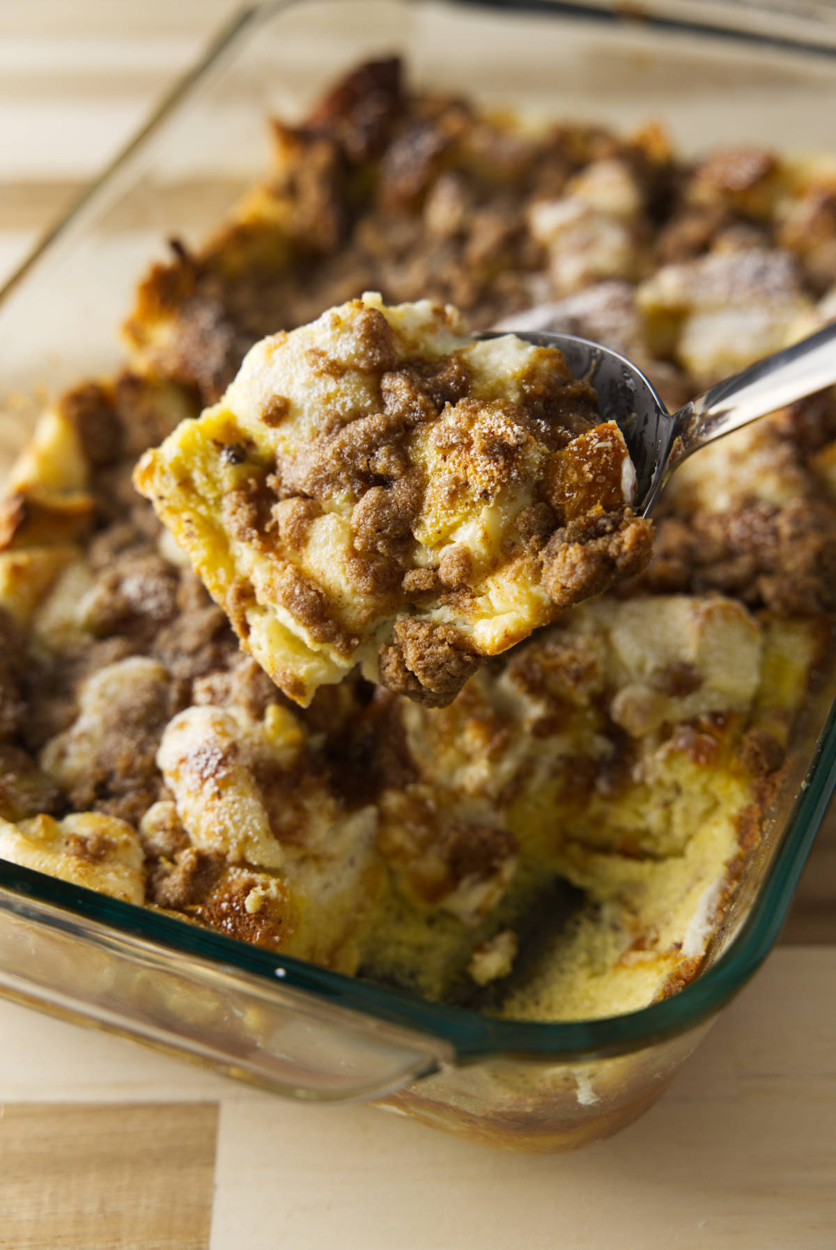 Baked French toast casserole in baking dish being scooped with large metal spoon.