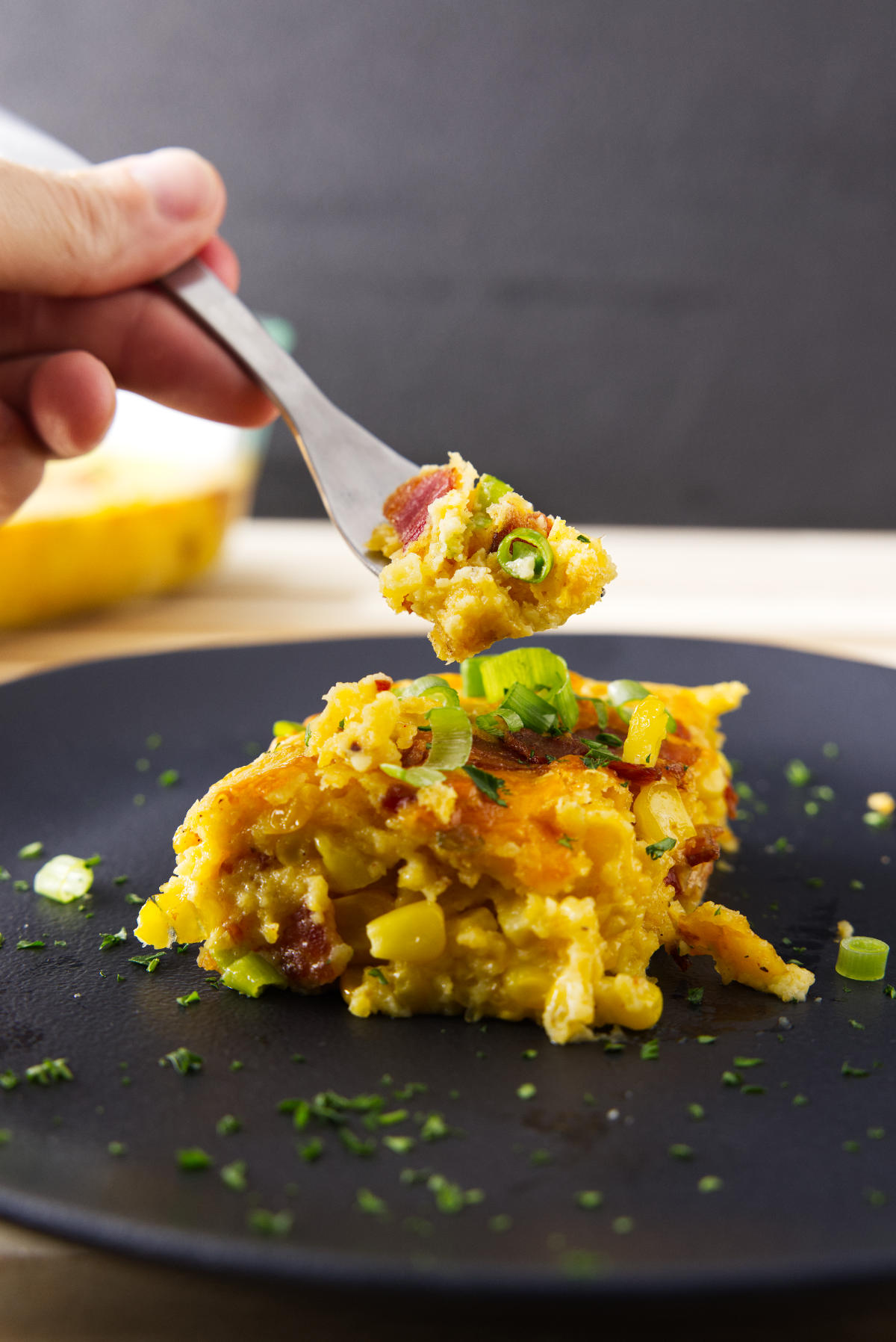 Fork with a bite of corn casserole lifting from black plate.