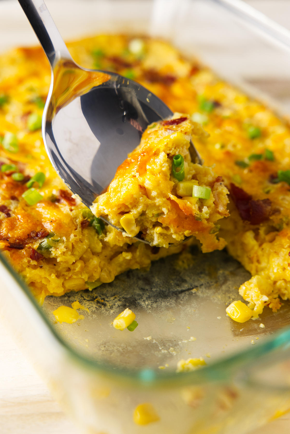Taking a large scoop of Smoked Corn Casserole from glass baking dish.