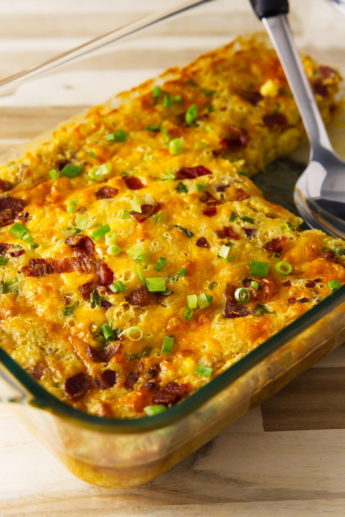 Corn casserole in baking dish with large serving spoon resting in the pan.