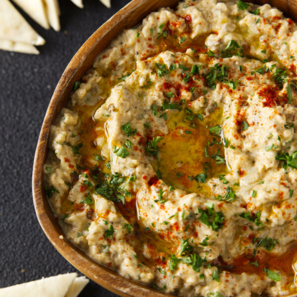 Overhead picture of smoked baba ganoush in a wooden bowl surrounded by slices of pita bread.