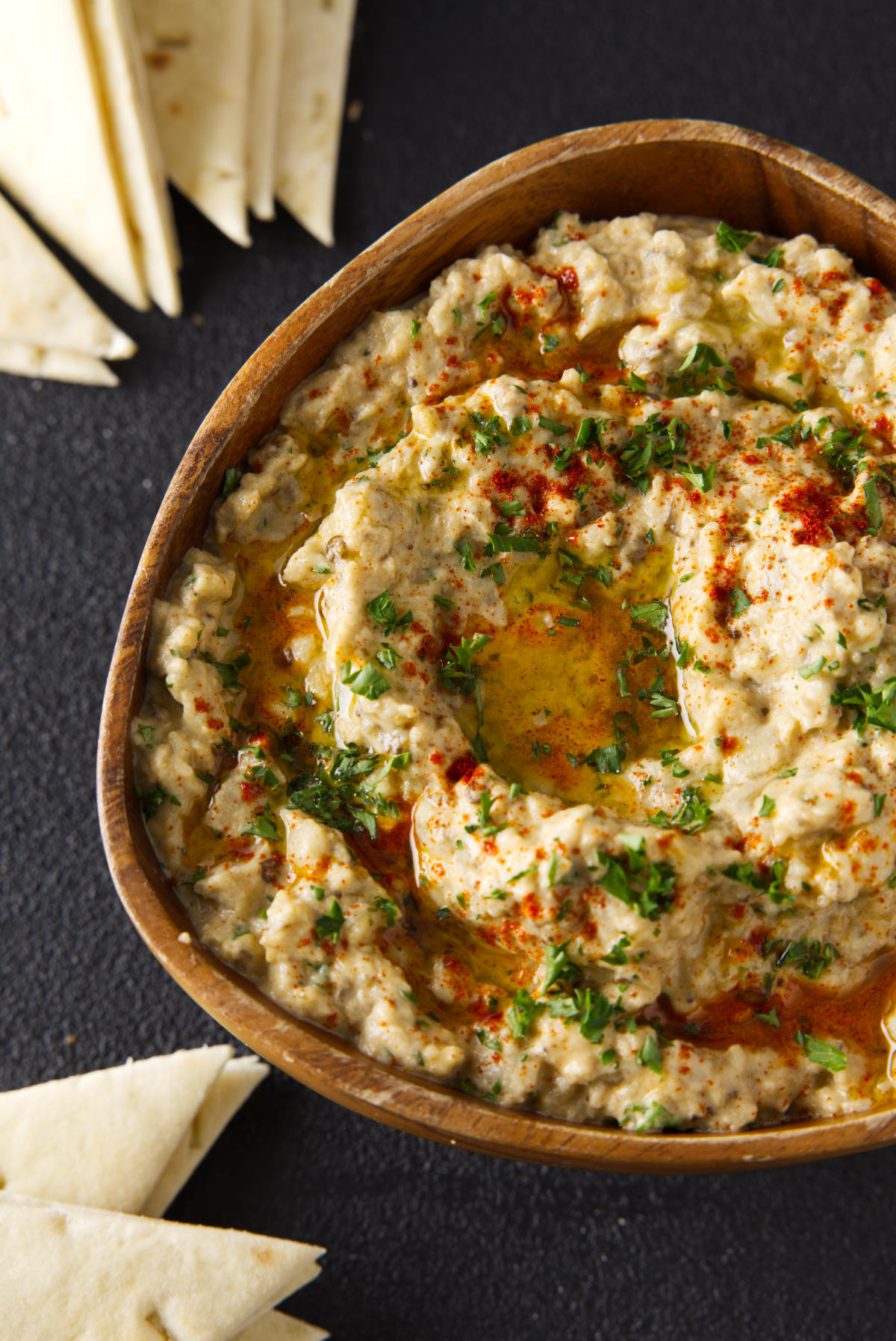 Overhead picture of smoked baba ganoush in a wooden bowl surrounded by slices of pita bread.