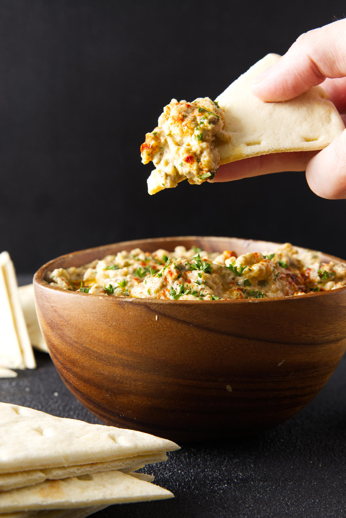 Dipping slice of pita bread in to a wooden bowl filled with baba ganoush.