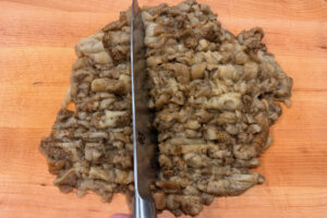 Chopping the flesh of roasted eggplants on a wooden cutting board.
