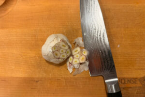 Cutting the top off of a bulb of garlic on a wooden cutting board.