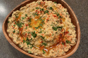 Wooden bowl filled with baba ganoush and topped with olive oil drizzle, chopped parsley, and a dusting of paprika.