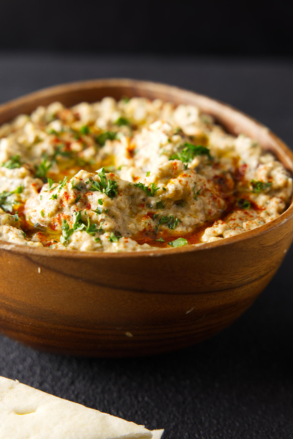 Smoked Baba Ganoush in a wooden bowl topped with chopped parsley and olive oil.