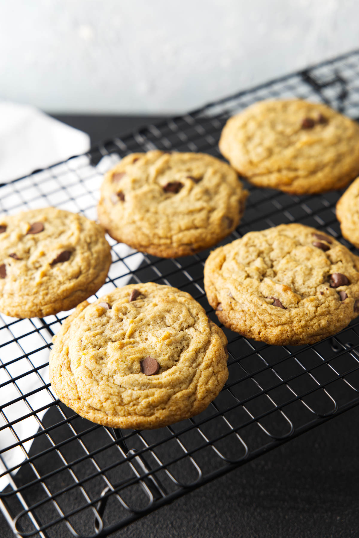 Six chocolate chip banana bread cookies cooling on a wire rack with white parchment paper on the table beneath.