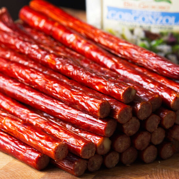 Snack sticks stacked on butcher block with gorgonzola cheese in background.