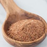 Large wooden spoon filled with brownish red cajun spice seasoning sitting on a marble table