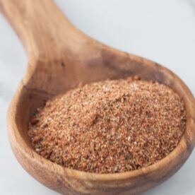 Large wooden spoon filled with brownish red cajun spice seasoning sitting on a marble table