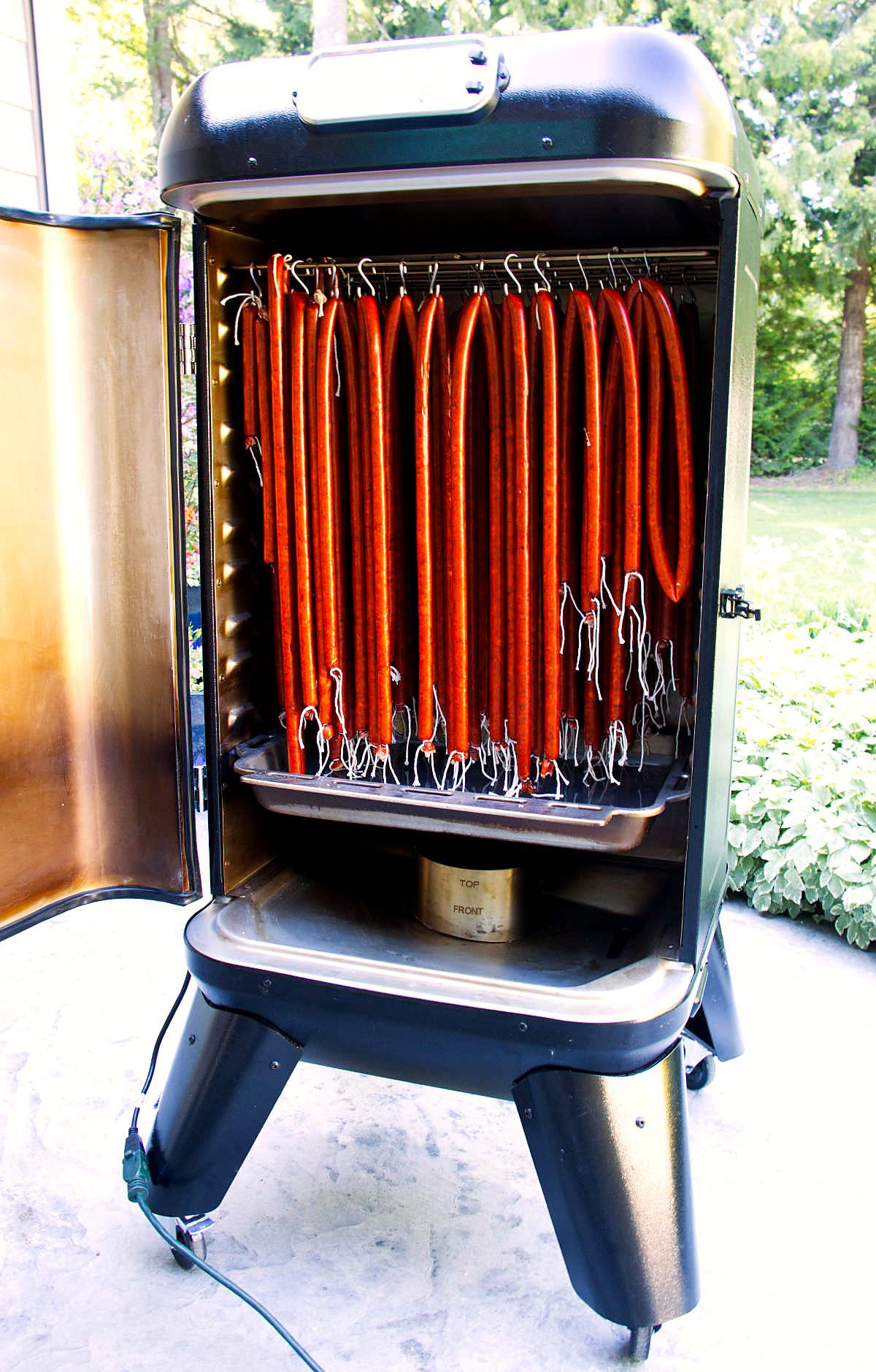 Venison snack sticks hanging on hooks in a vertical smoker.