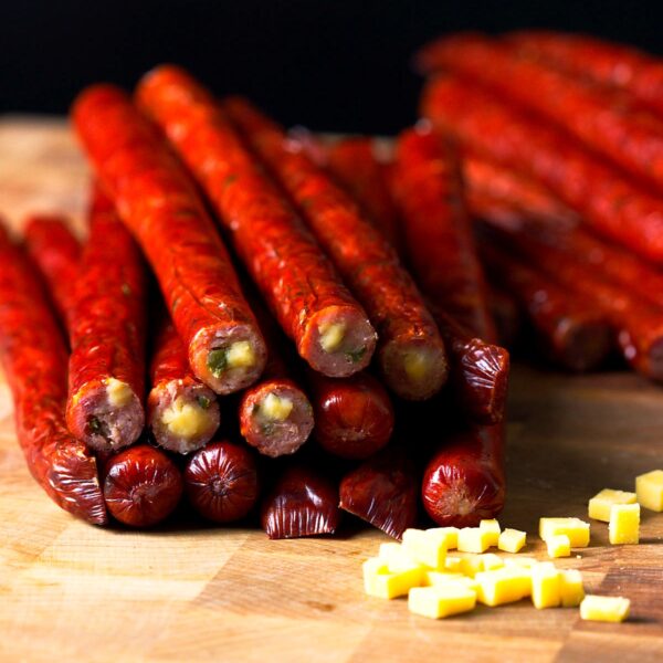 Smoked jalapeรฑo cheddar venison snack sticks stacked in a pile on a butcher block.