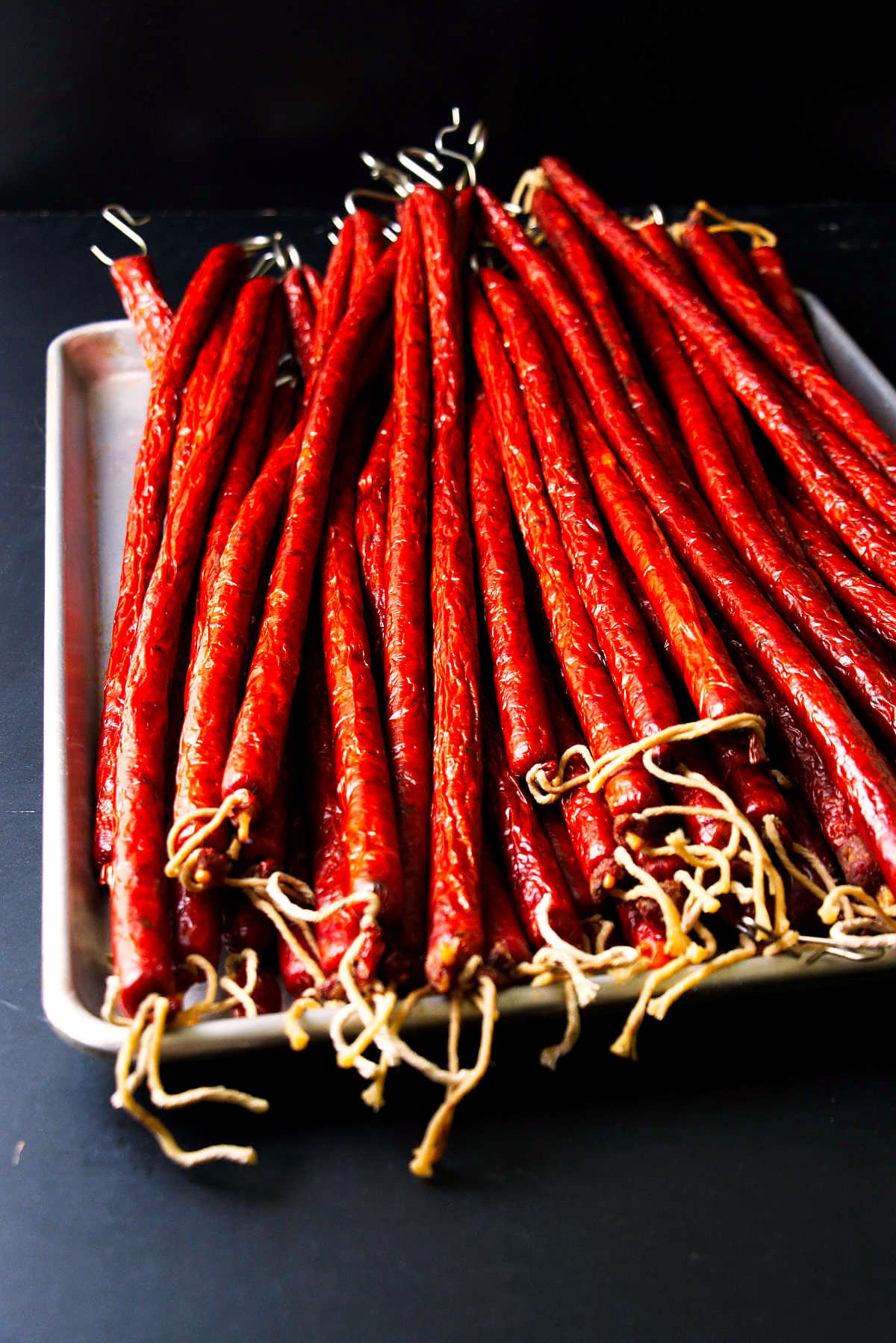 Venison snack sticks smoked and stacked on a stainless sheet pan.