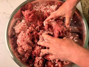 First mixing of the meat for smoked venison snack sticks in a large stainless bowl.