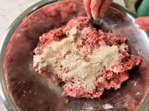 Adding dry ingredients to meat for venison snack sticks in a large mixing bowl.