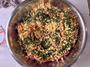 Adding jalapeños and cheddar cheese to meat in stainless mixing bowl.