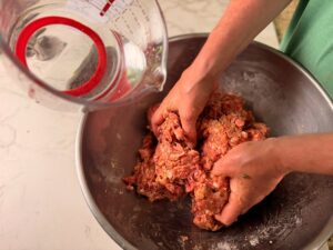 Adding water to the venison snack stick mixture.