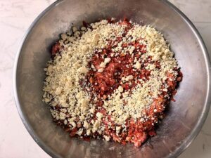 Sprinkling gorgonzola cheese over meat in a stainless steel bowl.