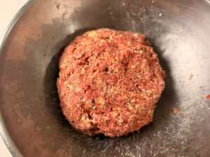 Mixing blue cheese bacon venison snack sticks meat in a stainless bowl.