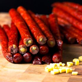Smoked jalapeño cheddar venison snack sticks stacked in a pile on a butcher block.