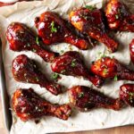 Several BBQ smoked chicken drumsticks coated in bbq sauce on parchment paper.