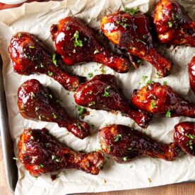 Several BBQ smoked chicken drumsticks coated in bbq sauce on parchment paper.