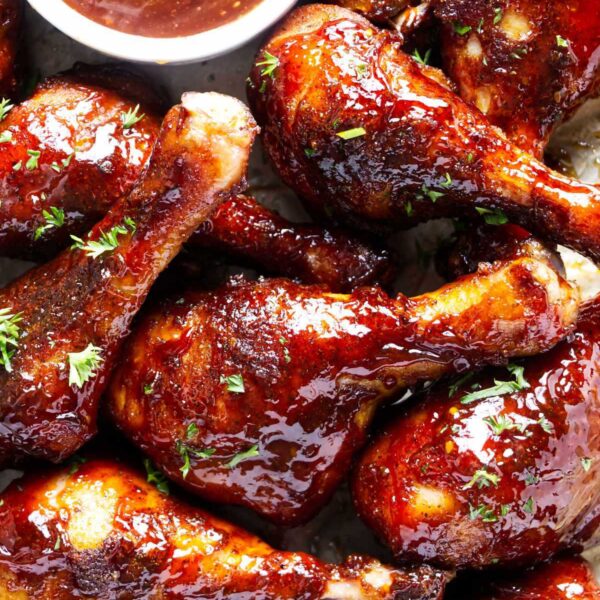 A pile of smoked chicken drumsticks coated in BBQ sauce on a serving platter.