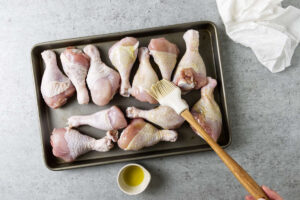 Brushing chicken drumsticks with oil.