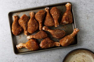 Coating chicken legs in a spice rub.