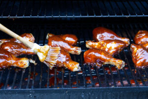 Chicken legs on a pellet grill getting brushed with bbq sauce.