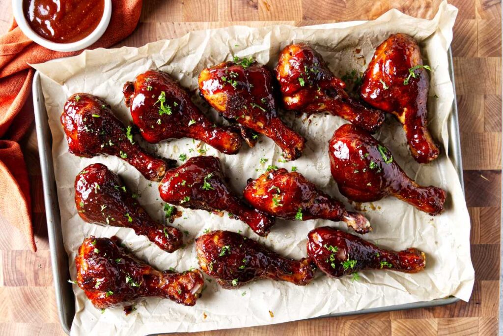 Several smoked chicken drumsticks on a cutting board coated in bbq sauce.