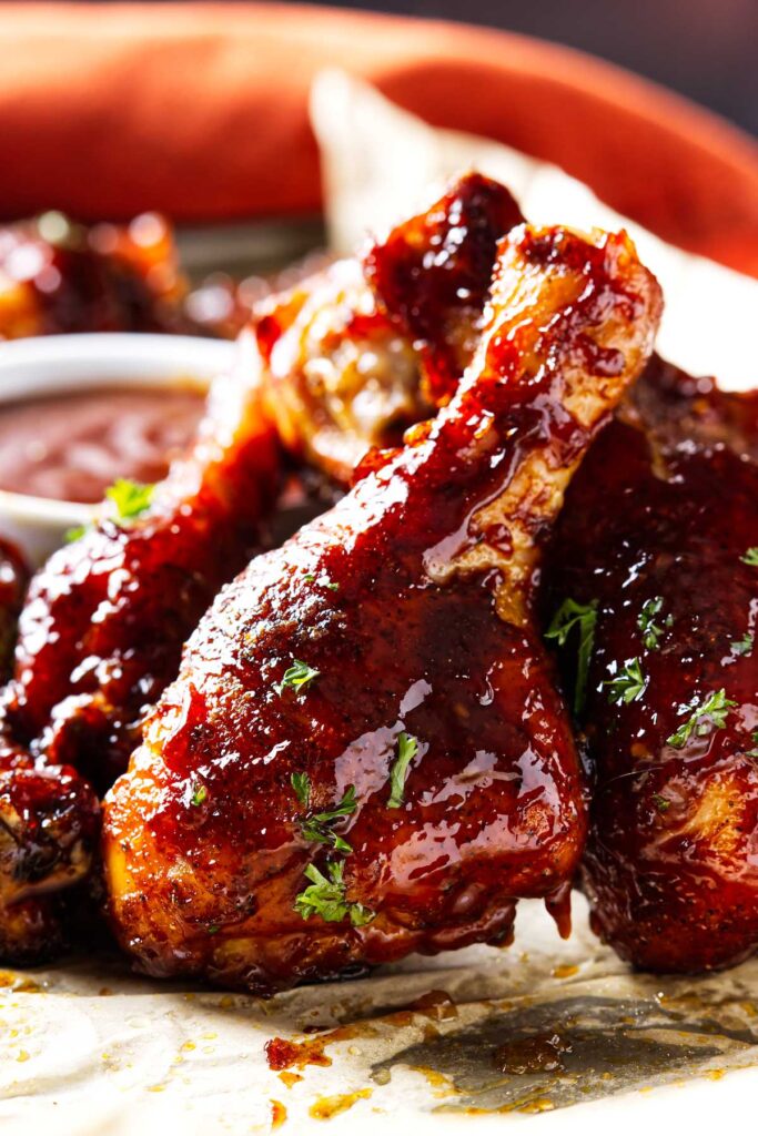 A smoked chicken leg sprinkled with fresh parsley in front of a dish of bbq sauce.