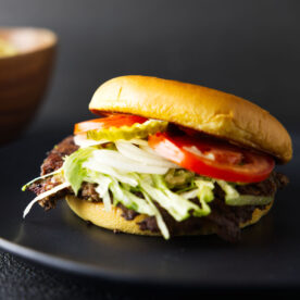 Closeup of Blackstone smash burger on a black plate loaded with toppings.